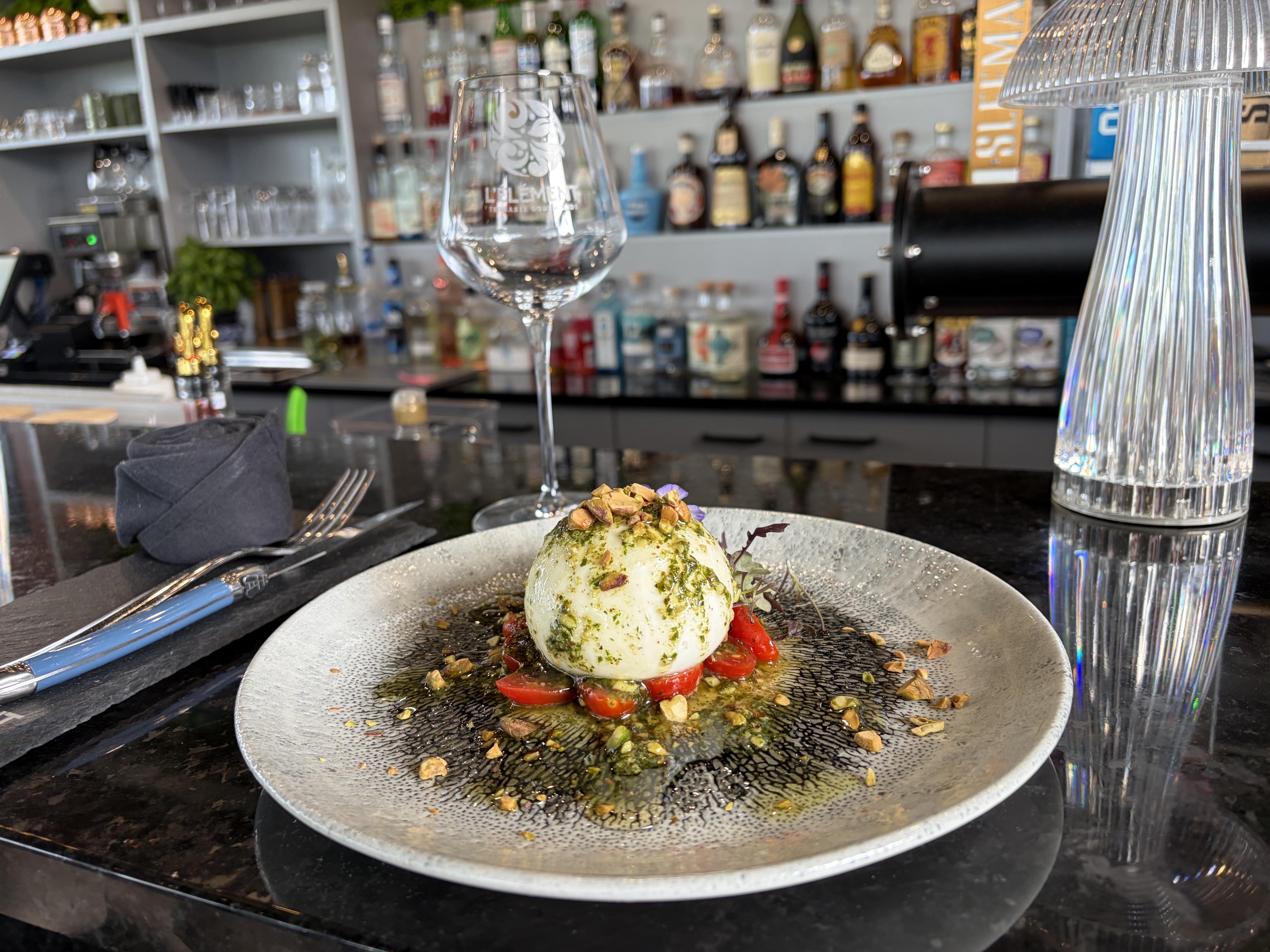 Burrata crémeuse au pesto, tomates et éclats de noisettes dressée au comptoir du bar