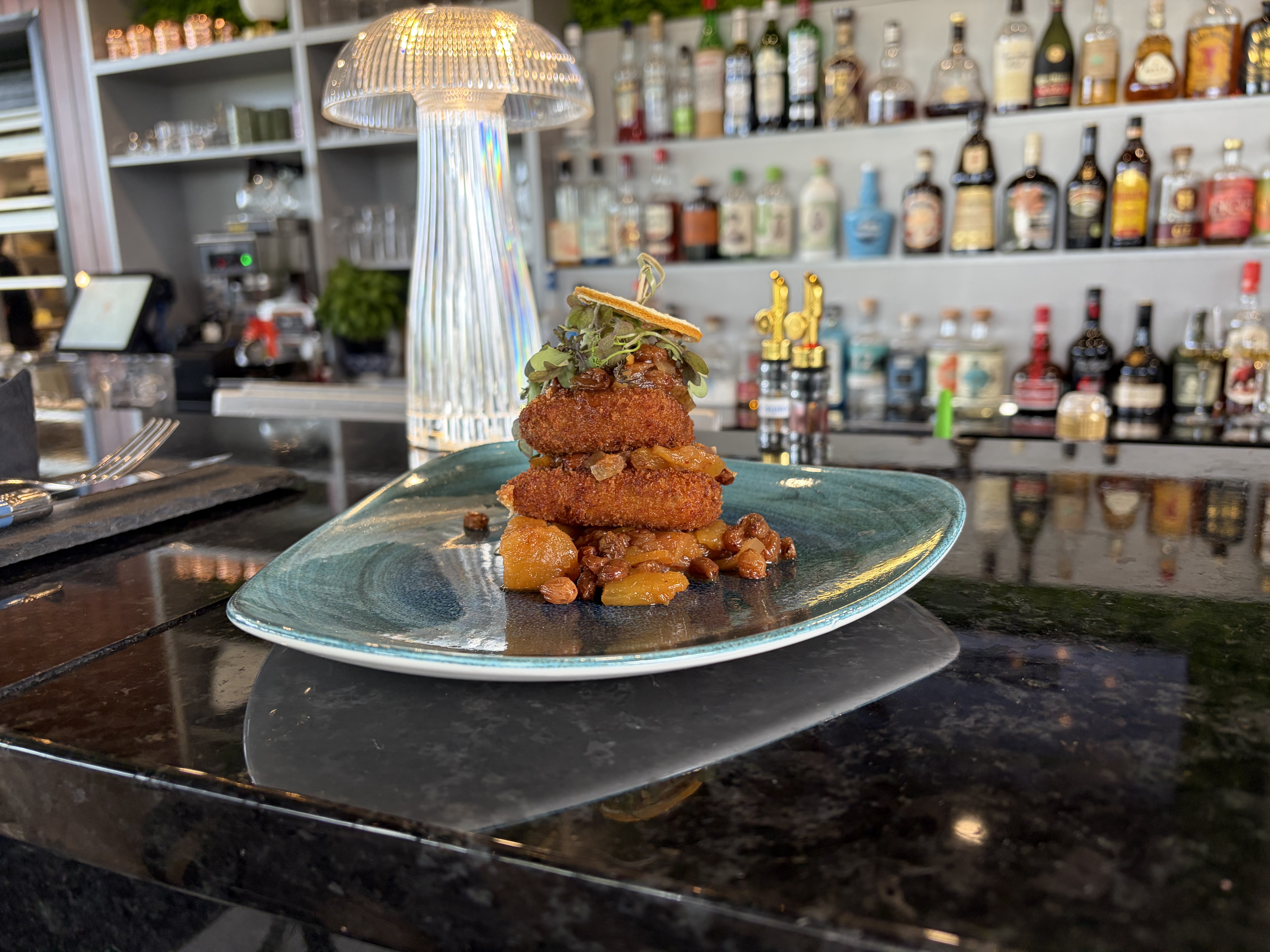 Croquettes croustillantes dressées en étage sur assiette turquoise au comptoir du bar