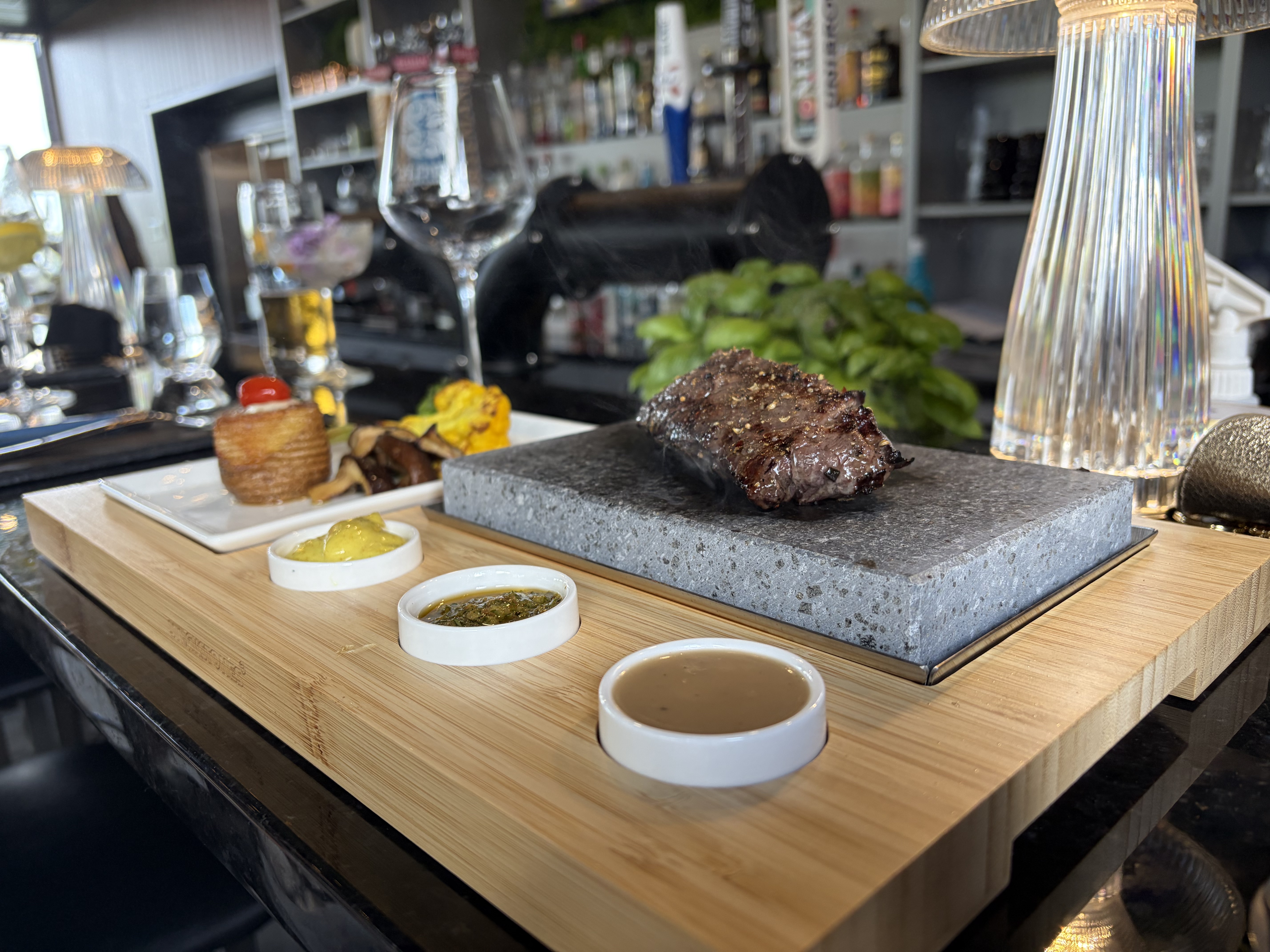 Pièce de bœuf saisie sur pierre chaude, servie sur planche de bois avec trio de sauces